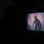 A person watches a horror video on a flickering screen with a spooky, dark background, creating a chilling atmosphere.
